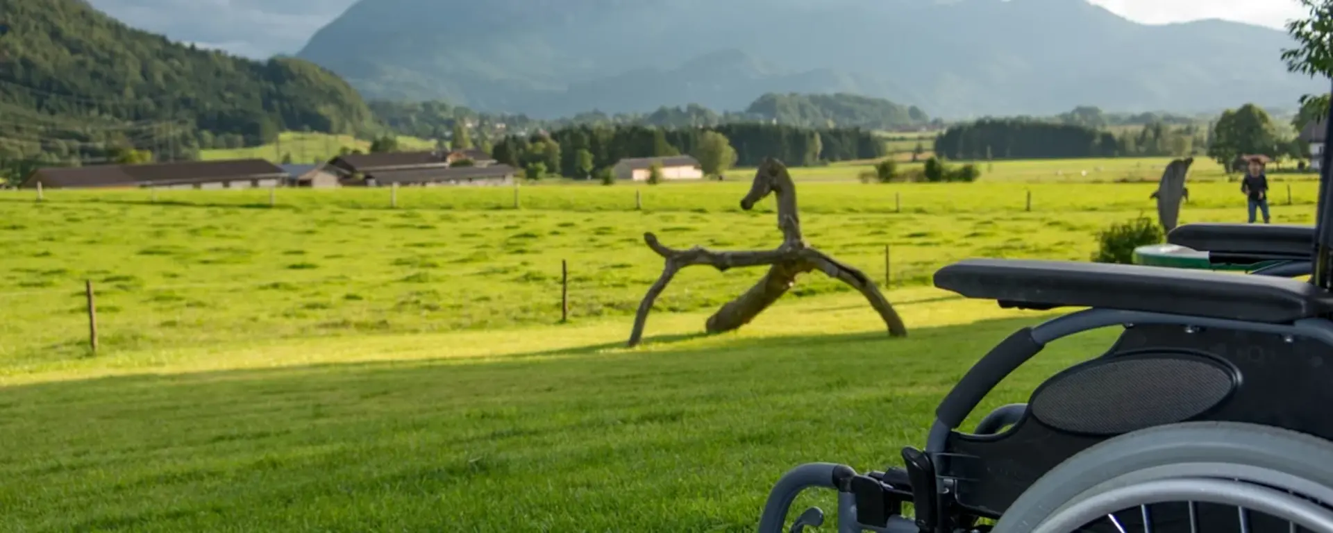 Barrierefreier Urlaub auf dem Bauernhof. Rollstuhl vor Bergpanorama