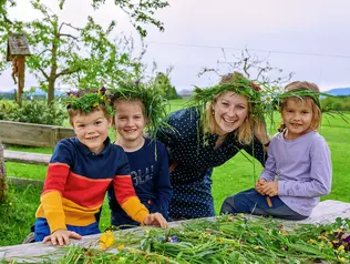 Gastgeberin bindet mit Gastkindern Blumenkränze