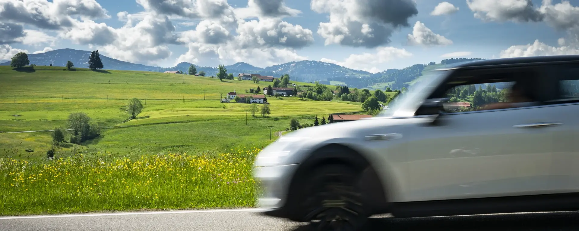 Fahrender weißer Mini vor Alpenpanorama auf der Deutschen Alpenstraße